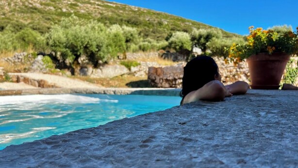 A stone ledge overlooking a pool with a view of a hillside.
