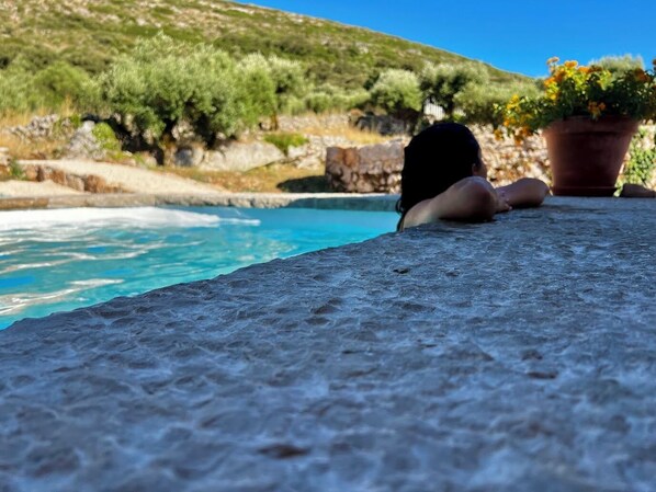 A stone ledge overlooking a pool with a view of a hillside.