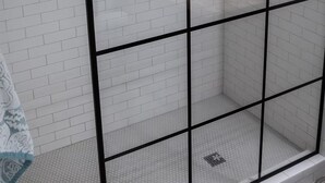 Zona de ducha con paredes y suelo de azulejos blancos, y cerramiento de vidrio.