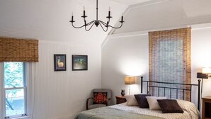 Un dormitorio con cama, una silla, una mesita de noche, una lámpara y una ventana con persianas.