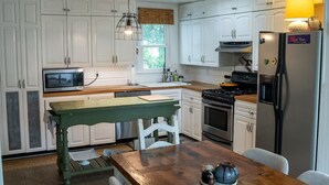 Una cocina con armarios blancos, una mesa de madera, estufa, microondas y refrigerador.