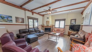 Ein Wohnzimmer mit Kamin, Ledersofas, Fernseher und Holzbalken an der Decke.