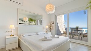 Ein Schlafzimmer mit Bett, Nachttischlampen, einem Spiegel und Blick auf den Strand.