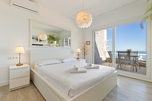 Un dormitorio con cama, lámparas de noche, un espejo y vista a la playa.