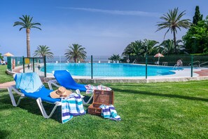 Zona de piscina con sillas de descanso, una sombrilla y una cesta de mimbre sobre el césped.