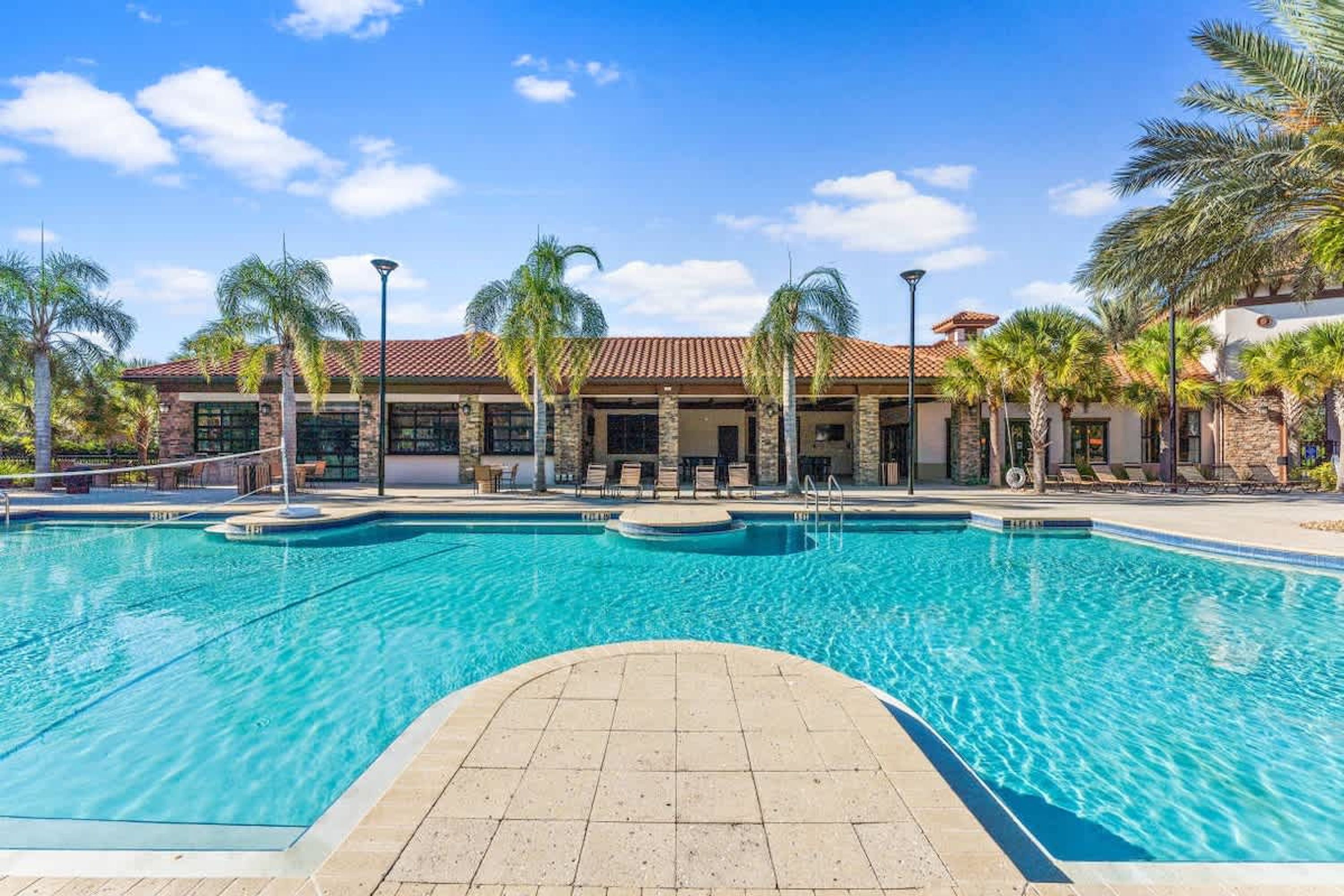 A swimming pool with a tiled deck, palm trees, and a building with a tiled roof.