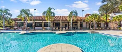 A swimming pool with a tiled deck, palm trees, and a building with a tiled roof.