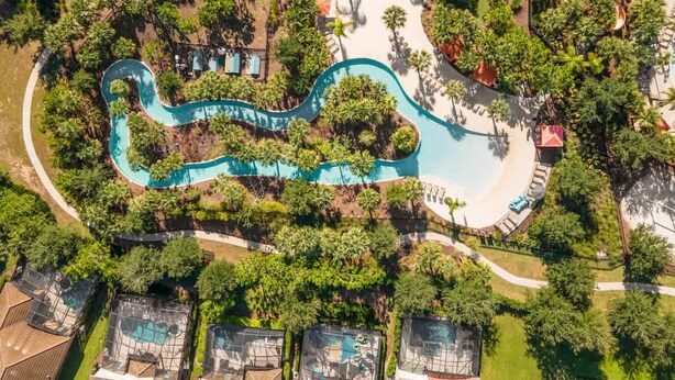 Eine Vogelperspektive zeigt ein Resort mit einem geschwungenen Pool, üppiger Vegetation und mehreren überdachten Bereichen.