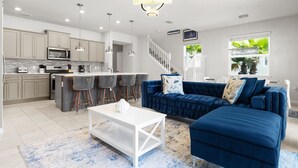 Eine moderne Küche mit einer zentralen Kochinsel, Barhocker und einem blauen Sofa im Wohnbereich.