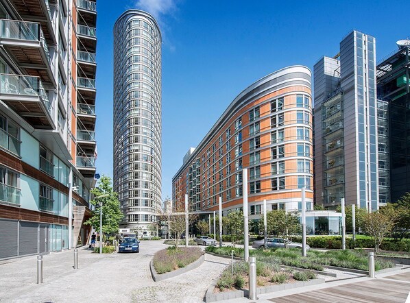 Ein moderner Stadtbaukomplex mit geschwungenen Baukörpern, einer Kombination aus Glas- und Backsteinfassaden sowie einem begrünten Innenhof mit Wegen und Pflanzen.