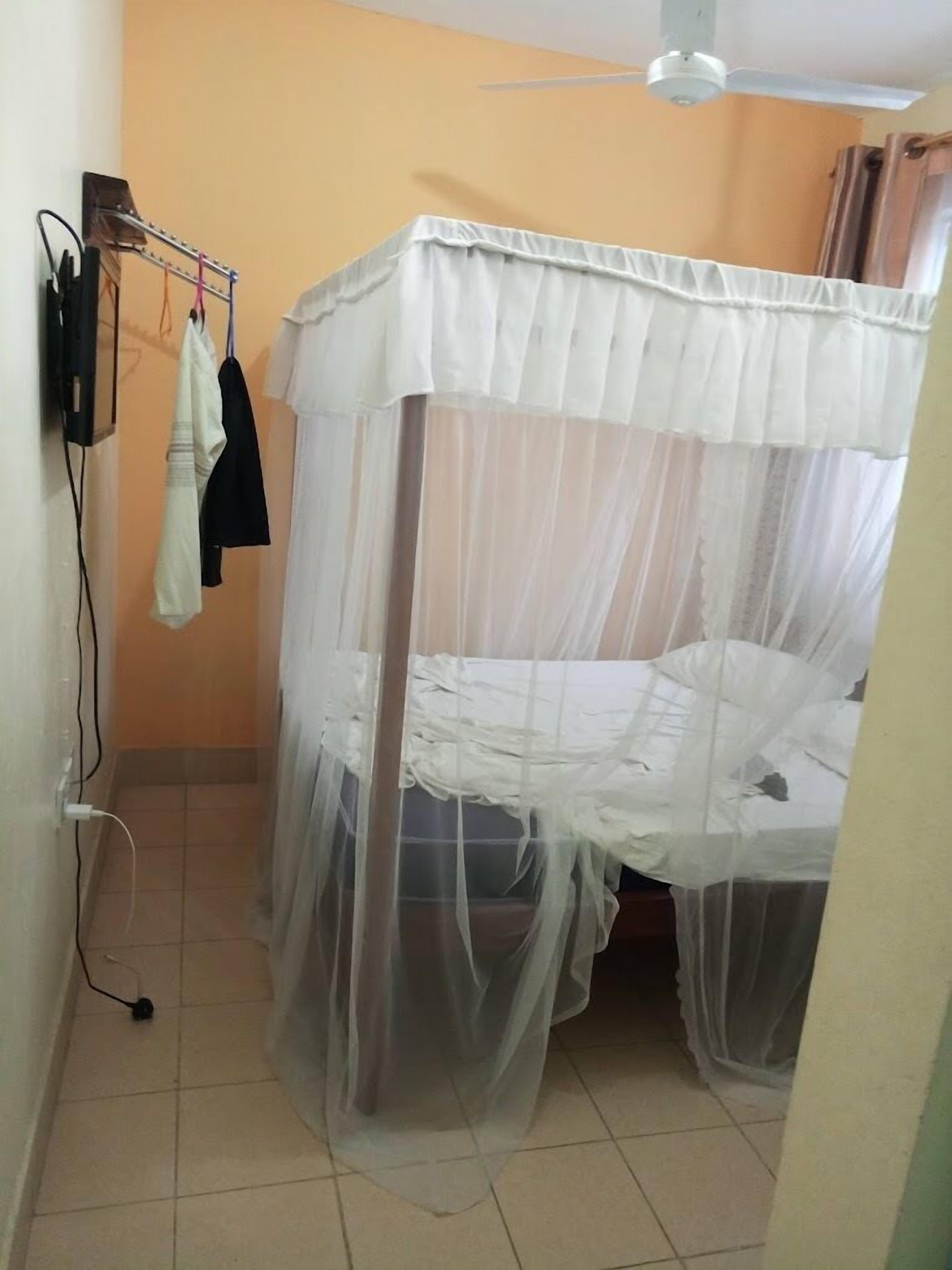 Habitación individual con mosquitera, ventilador de techo y televisor montado en la pared.