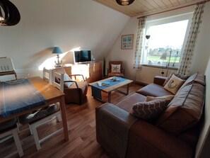 A cozy living room with a wooden floor, a brown sofa, a coffee table, a TV, and a dining area with a table and chairs.