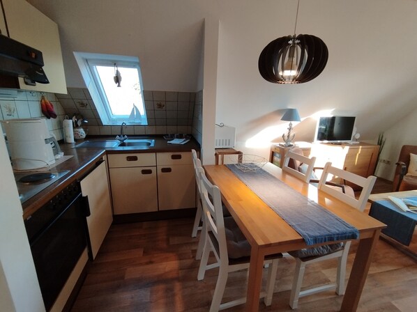 A compact kitchen with a wooden table and chairs, a built-in oven, and a window providing natural light.
