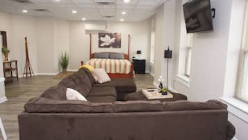 A modern living room with a large sectional sofa, a bed with a striped bedspread, and a mounted TV.