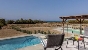 Un área junto a la piscina con vista al mar, una pérgola y una mesa con una botella y uvas.