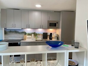 A modern kitchen with grey cabinets, a microwave, a coffee maker, and a beach-themed backsplash. - Family nest Waldblick - nature, peace, Eckernförde (Hütten)