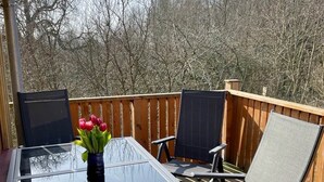 Une terrasse avec une table en verre, deux chaises et un vase rempli de fleurs.