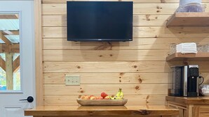 Une cuisine en bois avec un téléviseur fixé au-dessus du comptoir, un panier de fruits et une machine à café.