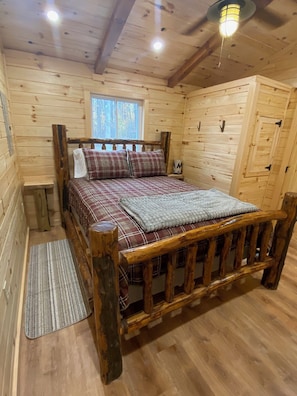 Una cama de madera con ropa de cama escocesa, un cabecero de madera y una mesita de noche con una lámpara.