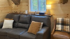 L’intérieur chaleureux d’un chalet avec un canapé en cuir, un fauteuil à carreaux et deux têtes de cerf empaillées accrochées aux murs.