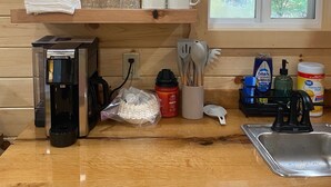 Une cuisine avec des étagères en bois où sont rangés de la verrerie, une machine à café et des ustensiles de cuisine.