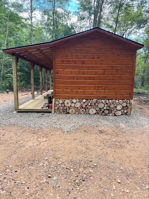 Una cabaña de madera con un porche y una pila de leña a la base.