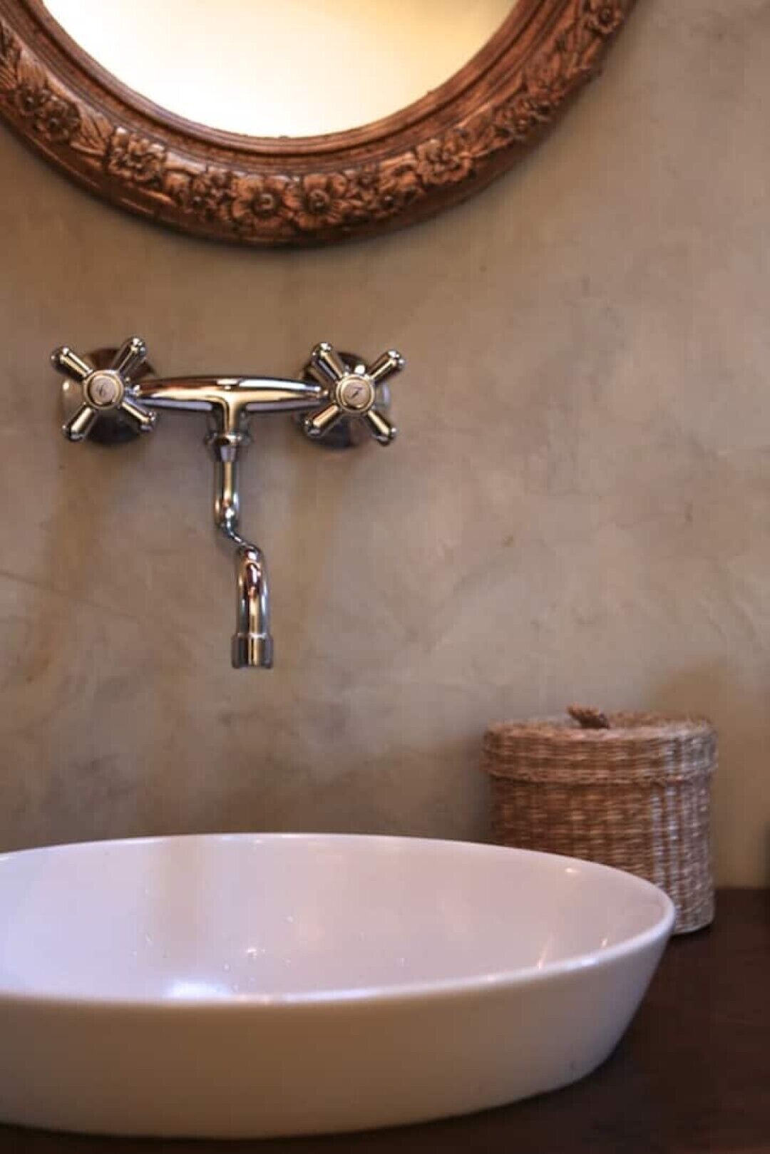 Un baño con lavamanos blanco, un grifo de pared y un espejo decorativo.
