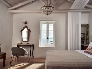 Une chambre avec un grand lit, un bureau en bois avec une chaise, un miroir et une fenêtre donnant sur la mer.