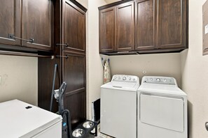 Une buanderie équipée de deux machines à laver blanches, d’un sèche-linge et d’un aspirateur.