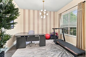 Une pièce comprenant un bureau, une chaise, un tapis de course, un ballon d’exercice et une plante en pot.