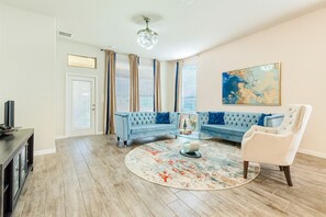 Ein Wohnzimmer mit einem blauen Sofa, einem weißen Sessel, einem Glastisch und einem runden Teppich.