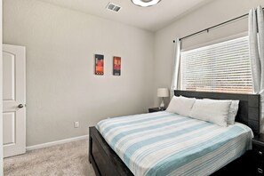 Ein Schlafzimmer mit einem Bett, einem Nachttisch, einem Fenster mit Jalousien und zwei Wandbildern.