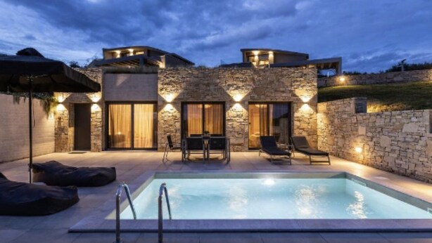 Une maison moderne dotée d’une piscine, de murs en pierre et d’un espace salon extérieur.