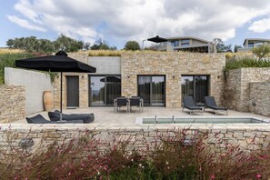 Un espace piscine extérieur moderne, agrémenté de murs en pierre, d’un coin salon et d’une terrasse couverte.