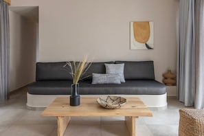 Un salon moderne avec un canapé gris foncé, une table basse en bois, un vase contenant des plantes séchées et une œuvre d’art géométrique accrochée au mur.