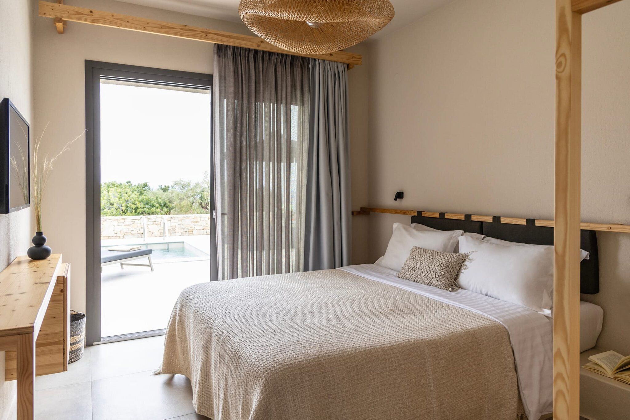 Une chambre dotée d’un grand lit, d’une tête de lit en bois, d’une table de chevet et offrant une vue sur un balcon avec une piscine.