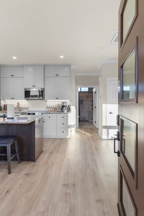 A modern kitchen with white cabinets, a central island, and a built-in microwave.