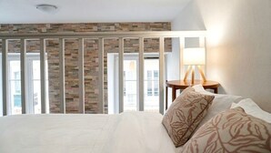Hotellihuone, jossa on suuri sänky, yöpöytä lampun kanssa ja ikkunasta avautuva näkymä kiviseinälle.