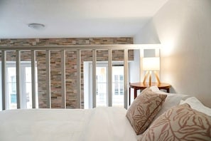 Een hotelkamer met een groot bed, een nachtkastje met een lamp en uitzicht door een raam met een stenen muur.