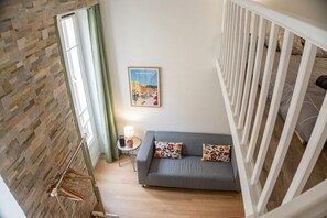 A room with a grey sofa, a wall-mounted picture, a hanging coat rack, and a window with curtains. - Authentic Nice Apartment, Walk to Shops & Dining (Nice)