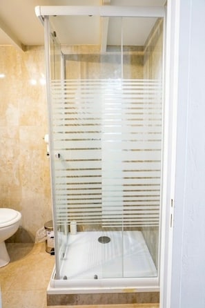 Een douchecabine met glazen wanden, een witte vloer en een beigekleurige betegelde muur.