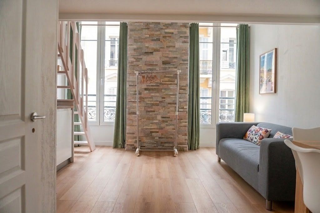 Ein Zimmer mit einem grauen Sofa, einer Steinwand und einem Fenster mit Vorhängen.
