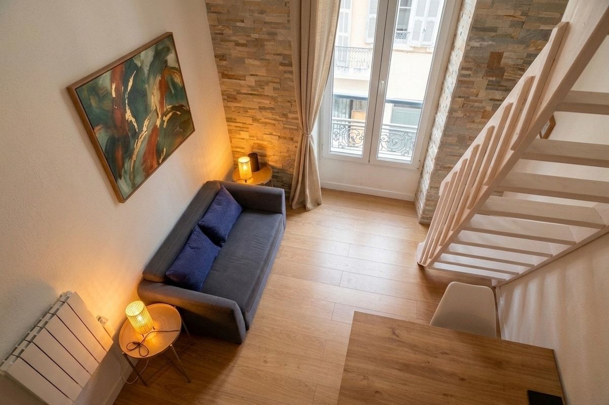 Un salon moderne avec un canapé, une petite table sur laquelle se trouve une lampe, un radiateur et un escalier menant à l’étage supérieur.