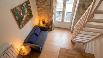 Un salon moderne avec un canapé, une petite table sur laquelle se trouve une lampe, un radiateur et un escalier menant à l’étage supérieur.