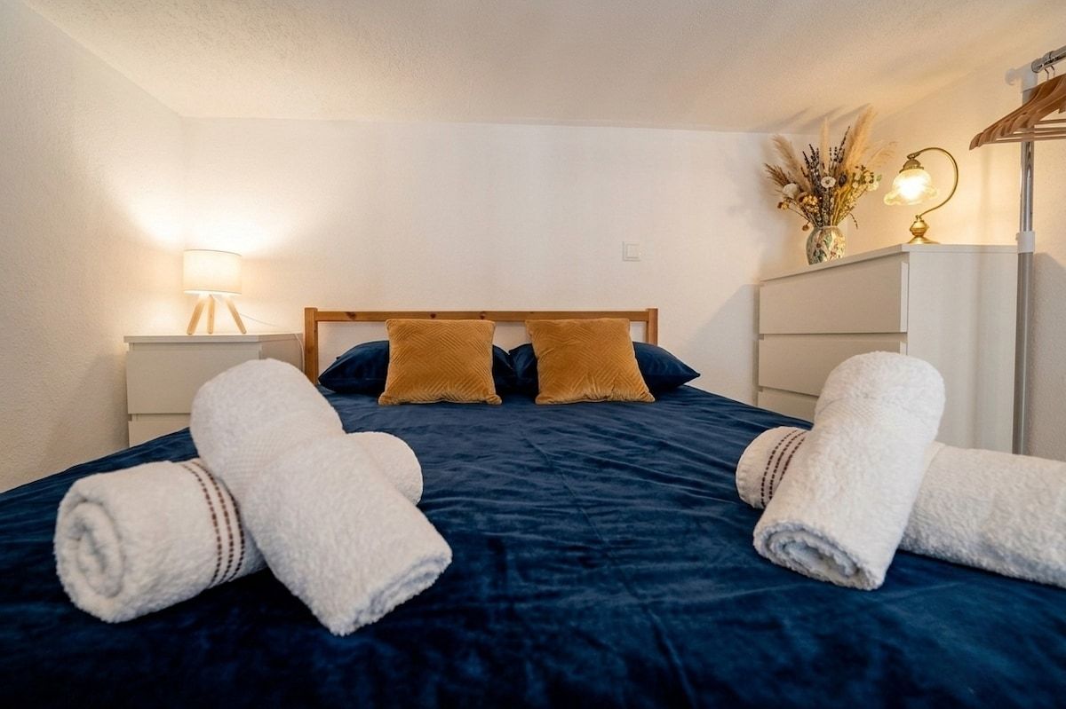 Une chambre d’hôtel avec un lit, deux oreillers, une table de chevet avec une lampe et une petite table à côté du lit avec un vase.