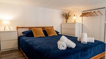 Un lit bien fait, recouvert d’une couvre-lit bleu foncé, avec deux oreillers et des serviettes enroulées, le tout posé sur un cadre en bois.