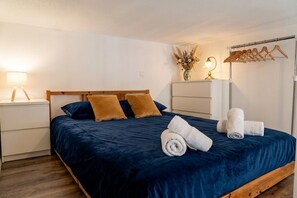 A neatly made bed with a dark blue bedspread, two pillows, and rolled towels on a wooden frame. - Le Siagre - 5min à pied de la gare (Nice)