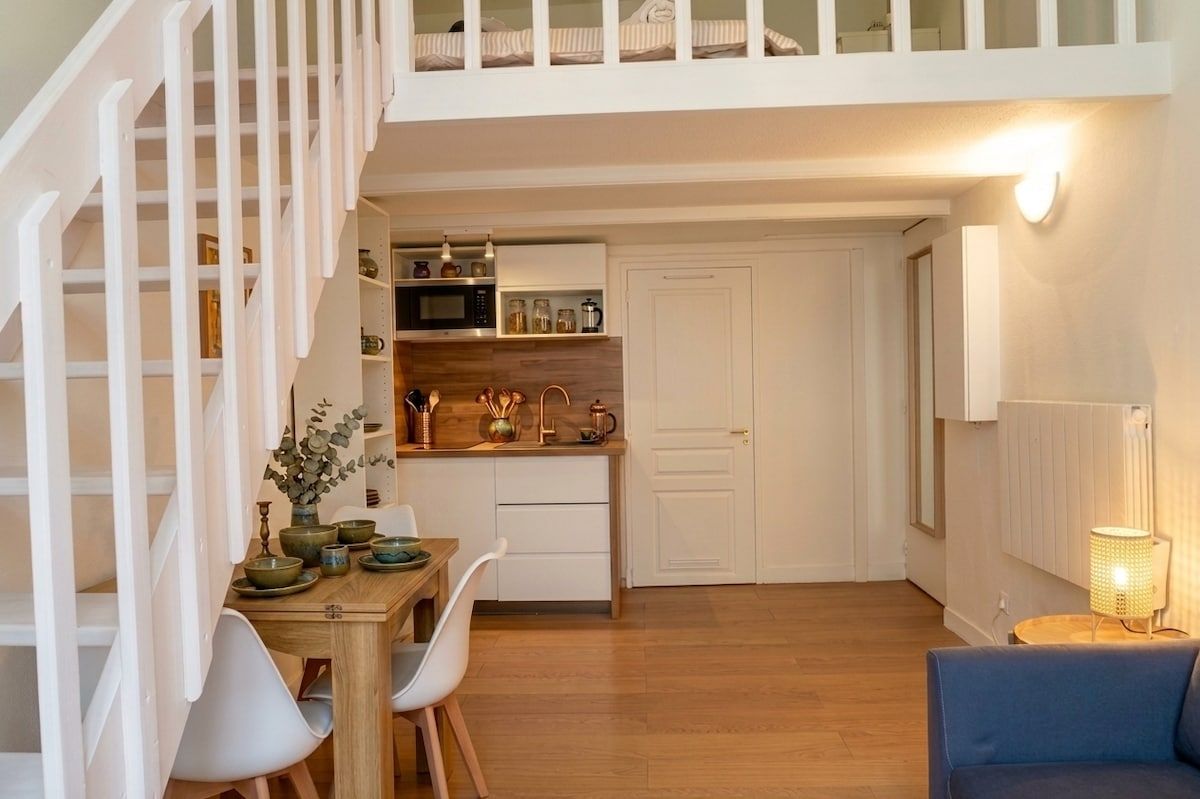 A modern kitchen with white cabinetry, a dining area with a wooden table and chairs, and a staircase with white railings.