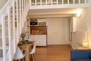 Cozinha moderna com armários brancos, área de jantar com mesa e cadeiras de madeira, e escada com corrimão branco.