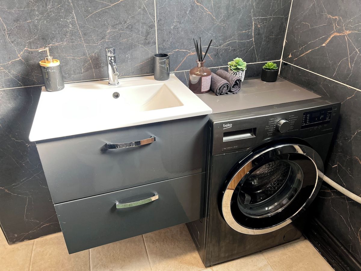 Une petite salle de bain comprenant un lavabo, un lave-linge et un meuble avec des tiroirs.